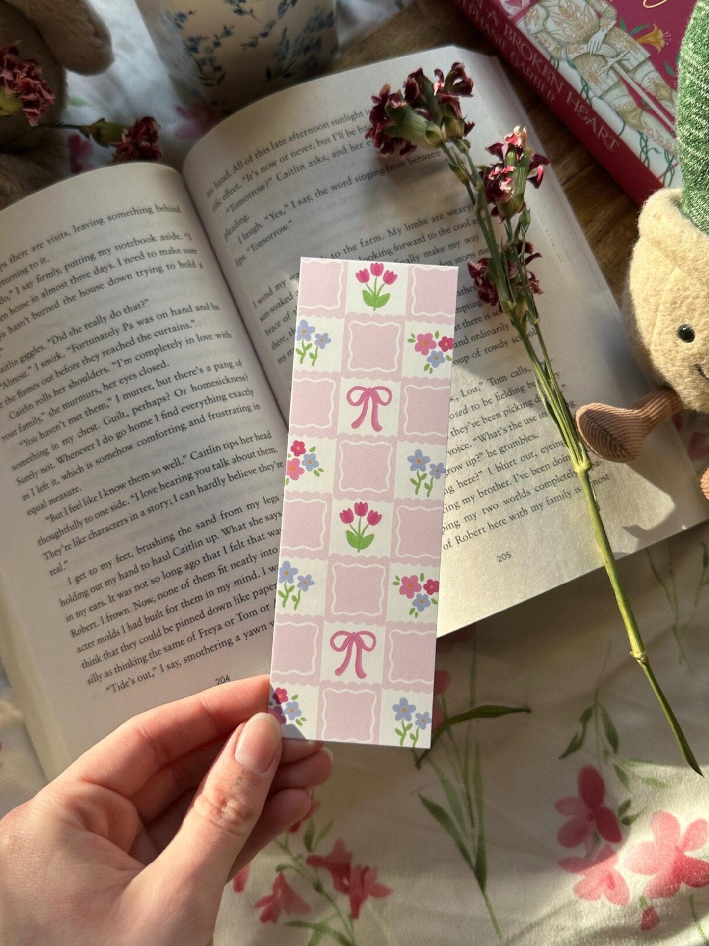 Hand holding a decorative bookmark over an open book with a floral patterned background.